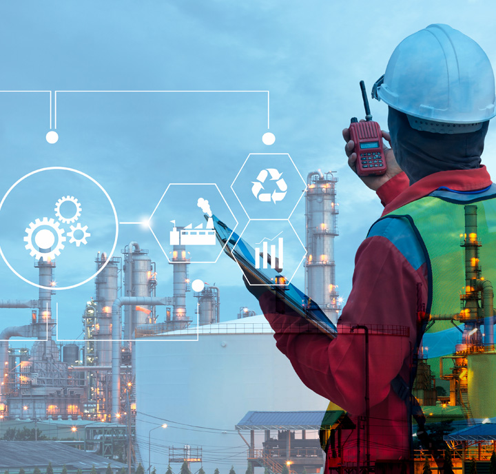 A worker in a hard hat and safety vest holds a tablet and radio, facing an industrial site with tall chimneys. Overlaid icons include gears, a factory, a bar chart, and a recycling symbol, set against a twilight sky. The scene suggests industrial operations and communication.