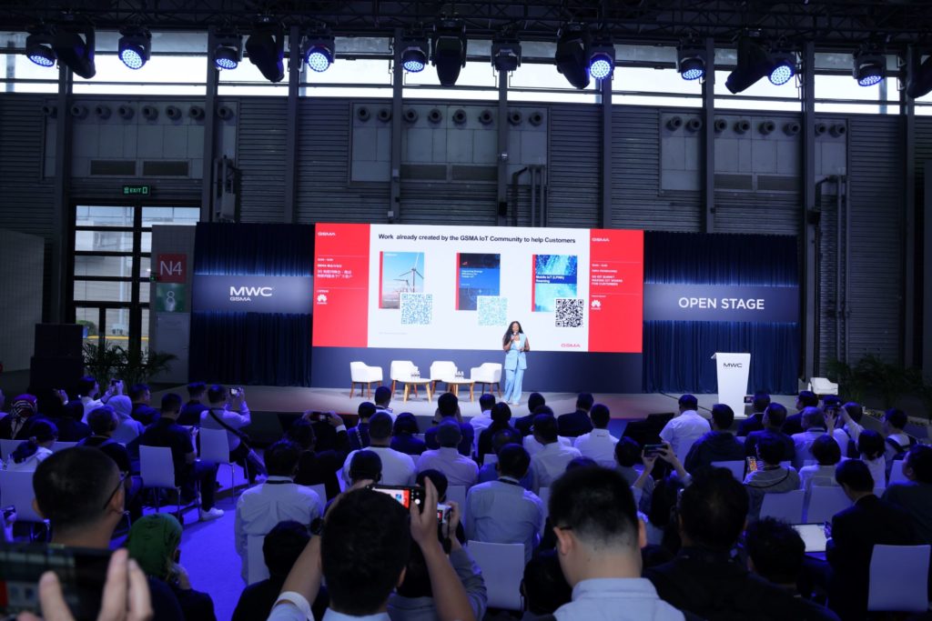 A woman on stage speaking on stage to a room full of people 