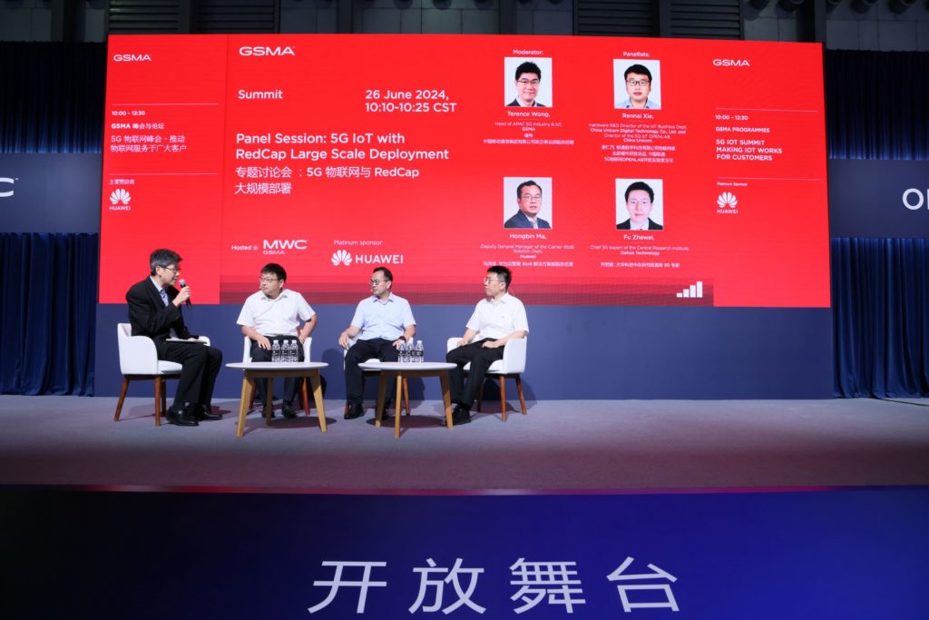 4 men on stage sitting down talking to each other with a big screen behind them.