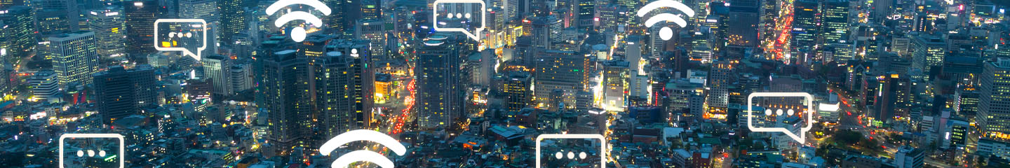 Aerial view of a brightly lit cityscape at night, with illuminated skyscrapers and busy streets. Digital icons for chat bubbles and Wi-Fi signals are overlaid, representing digital communication and internet connectivity throughout the city.