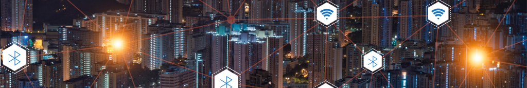 A cityscape at night with tall, illuminated buildings. Orange light flares and glowing lines connect Wi-Fi and Bluetooth icons, representing digital connectivity and smart technology integration across the urban environment.