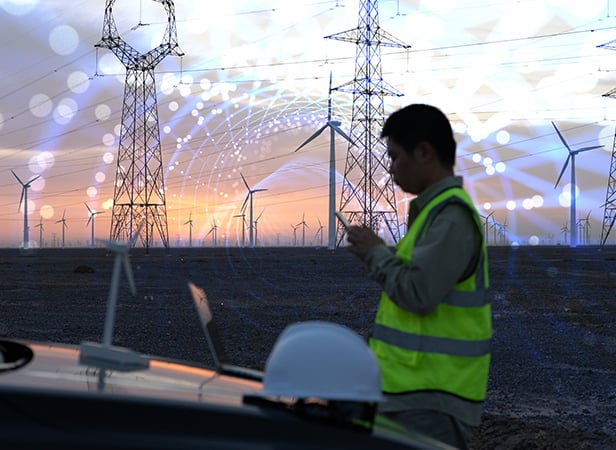 Silhouette of a worker with wind turbines and power lines at sunset, with digital network graphics overlay.