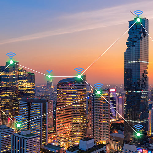 City skyline at sunset with connected lpwan network icons and lines over buildings, representing smart technology.