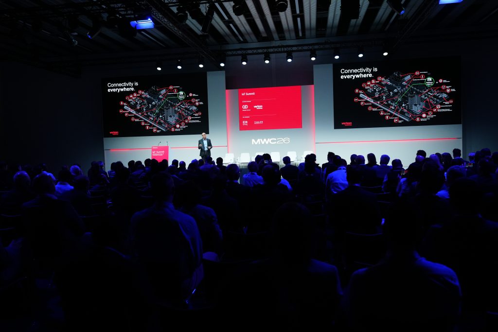 A speaker presents on stage at MWC, with slides showing "Connectivity is everywhere" to an audience.