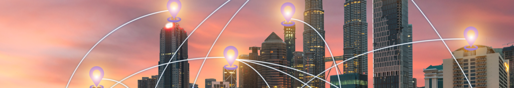 A modern city skyline at sunset with tall skyscrapers. Glowing icons and curved white lines overlay the image, connecting the buildings, symbolizing digital connectivity or communication networks. The sky is a blend of pink and orange hues.