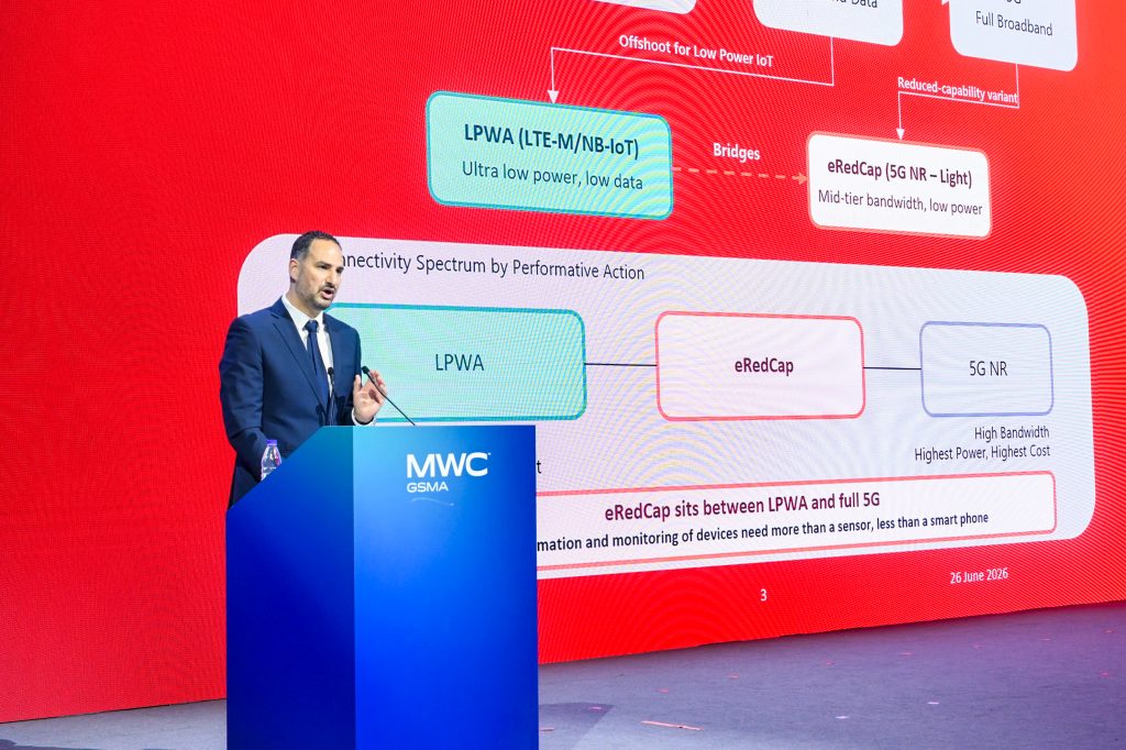 A man in a suit speaks at a podium labeled "MWC GSMA" onstage. Behind him, a large red and blue screen displays a connectivity diagram comparing LPWA, eRedCap, and 5G NR technologies, with detailed text and arrows explaining each category.