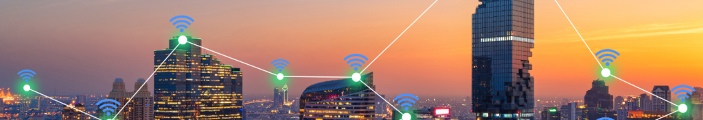 A city skyline at sunset with tall buildings. Blue and green Wi-Fi symbols are connected by glowing lines, illustrating wireless network connectivity across the urban landscape. The sky is orange and purple, and windows are illuminated.