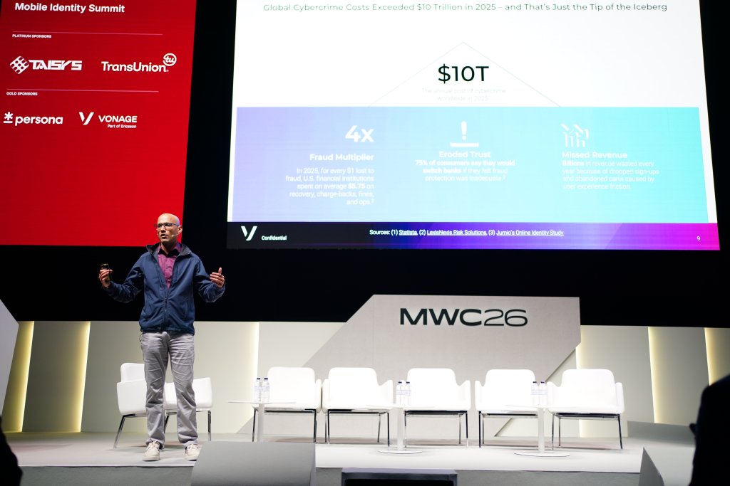 A speaker presents on stage at MWC26 with a cybercrime cost slide displayed on a large screen behind him.