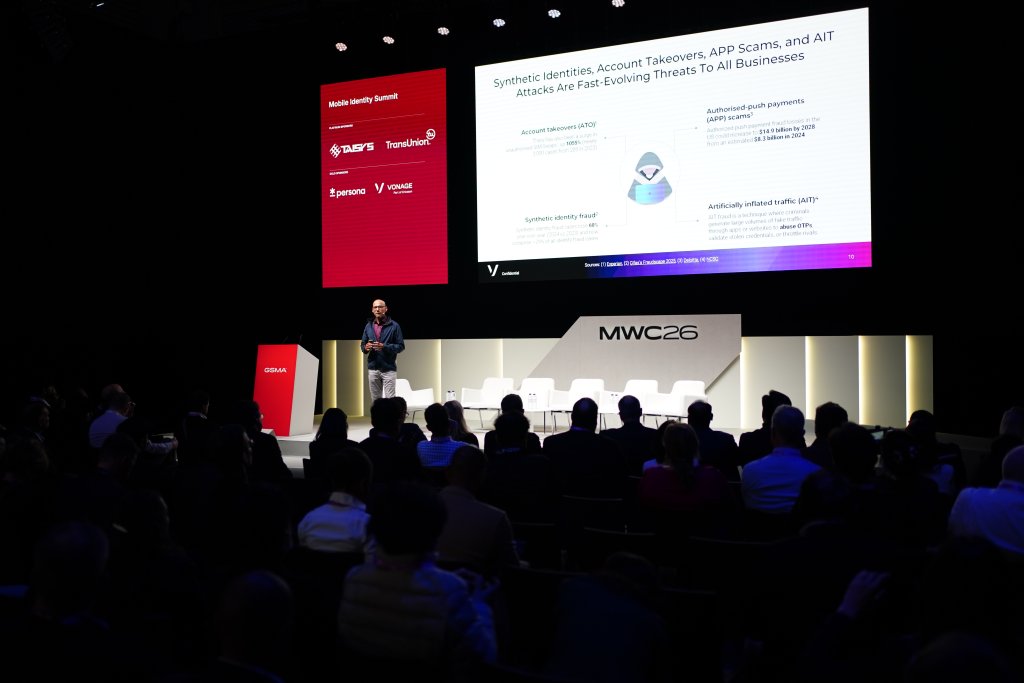 A speaker presents on digital security threats to an audience at a tech conference, MWC26, with slides displayed.