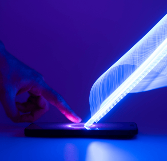 A finger touches a smartphone screen, creating a bright, glowing trail of blue light that arches upward in a long exposure effect. The background is a solid, deep purple.