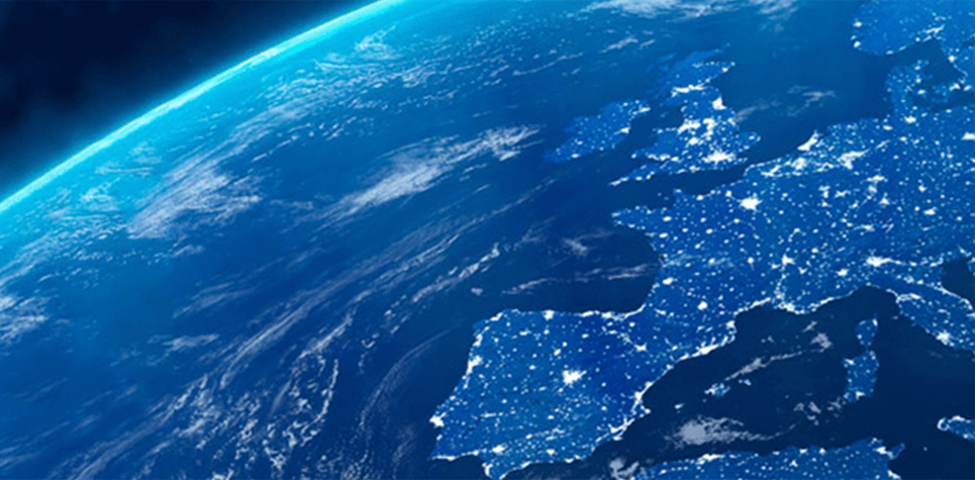 A view of Earth from space, showing Europe at night. The continent is illuminated with numerous bright lights indicating populated areas. The surrounding ocean is dark, and the curvature of the planet is visible along with a faint blue atmosphere at the horizon.
