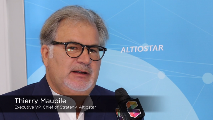 A person with gray hair and glasses is speaking into a microphone. They are wearing a dark suit and light shirt, standing in front of a blue background with the word "Altiostar." Text on the image reads: "Thierry Maupile, Executive VP, Chief of Strategy, Altiostar.