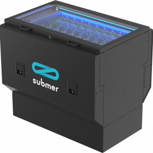A black, rectangular computer server immersion cooling system with a transparent top, revealing components immersed in liquid. It has a prominent logo on the side with a stylized infinity symbol and the word "submer" below it. The interior is illuminated with blue lighting.