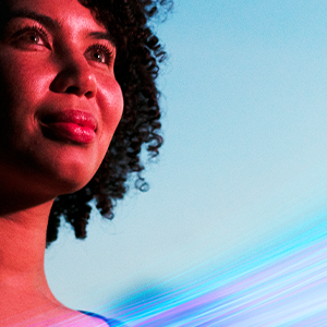 A person with curly hair gazes upward with a hopeful expression. The background is a clear blue sky, and there is a dynamic, colorful light effect at the bottom, adding a sense of motion and energy to the image.