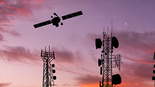 Silhouetted against a sunset sky, telecommunications towers are prominently featured. A moon crescent is visible on the right, while a satellite with extended solar panels is flying across the sky. The background is a gradient of orange to purple, accentuated by wispy clouds.