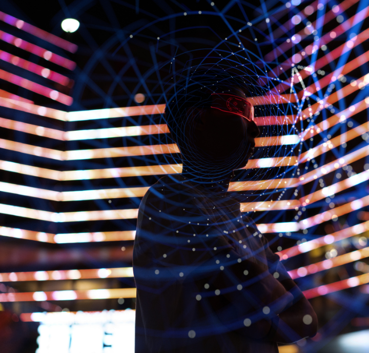 A person stands with arms crossed in front of vibrant, colorful LED light strips. Their face is mostly in shadow, wearing glowing glasses. Blue concentric geometric lines are superimposed, giving a futuristic, digital effect to the image.