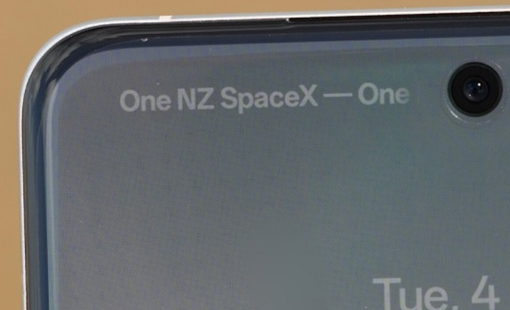 Close-up of the top part of a smartphone's screen showing the network name "One NZ SpaceX — One" near the front-facing camera, indicating connectivity. The edge of the device and part of the display are visible against a plain background.