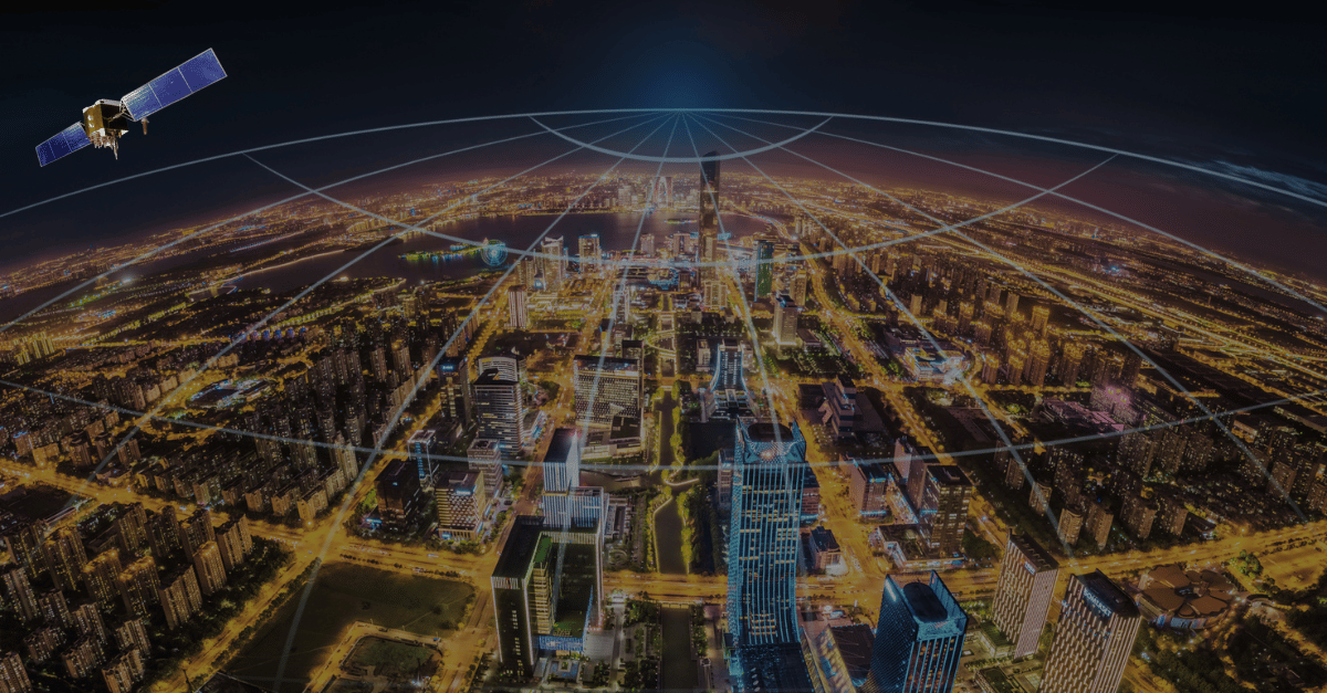 A cityscape at night is brightly lit with buildings and streets. A satellite hovers in the upper left sky, emitting curved white signal lines that extend over the entire city, illustrating the concept of satellite communication or connectivity.