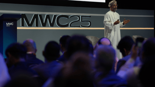 A man in traditional Omani dress speaks on stage at MWC25, with a seated audience in the foreground. The MWC25 logo is prominently displayed behind him on a modern, dark-colored backdrop.