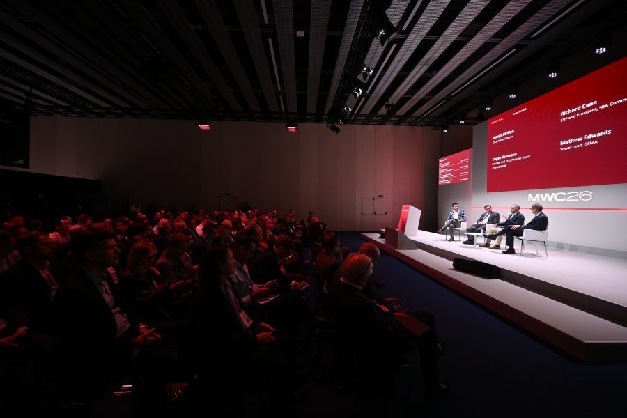 A panel discussion takes place on stage at MWC26, with a large audience seated in a dark conference room.