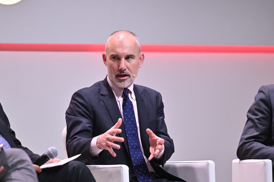Man in a suit speaking passionately on a panel, gesturing with his hands, microphone on his cheek.