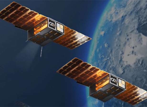 Two small cube-shaped satellites with solar panels orbit above Earth.
