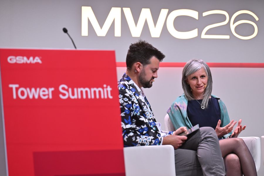 Two people speaking on stage at the Tower Summit during MWC26, with a red event sign in the foreground.