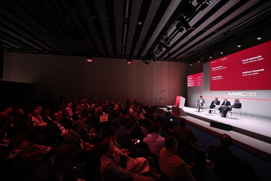 A panel discussion takes place on stage at a conference, with an audience seated and watching attentively.