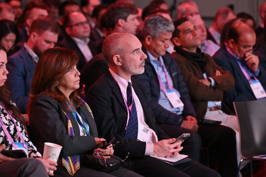 A group of people in business attire sit attentively in an audience at a conference or seminar.