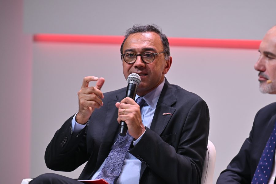Man in a suit speaking into a microphone whilst gesturing with his hand during a panel discussion.