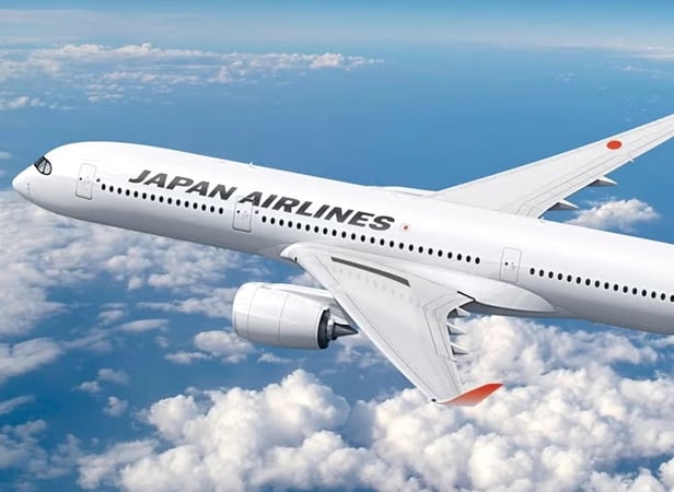 A Japan Airlines aeroplane flying above the clouds in a bright blue sky.