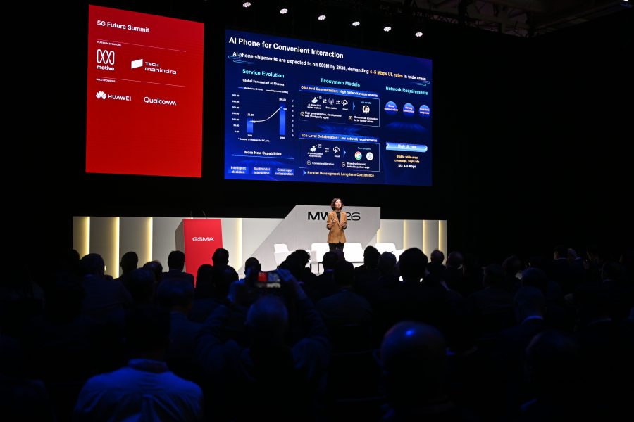 A speaker presents on AI mobiles at a tech summit, with slides displayed to an audience in a dark auditorium.