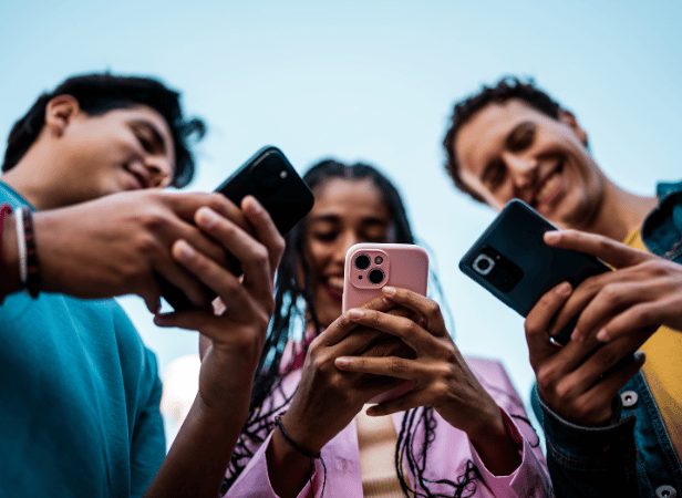 Three people smiling and looking at their mobiles, photographed from a low angle against a blue sky.