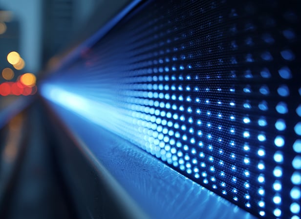 Quantum computing. Close-up view of a curved LED display emitting bright blue and white lights in rows, creating a futuristic, glowing effect. The background is softly blurred with hints of city lights, producing a bokeh effect and emphasising the illuminated panel.