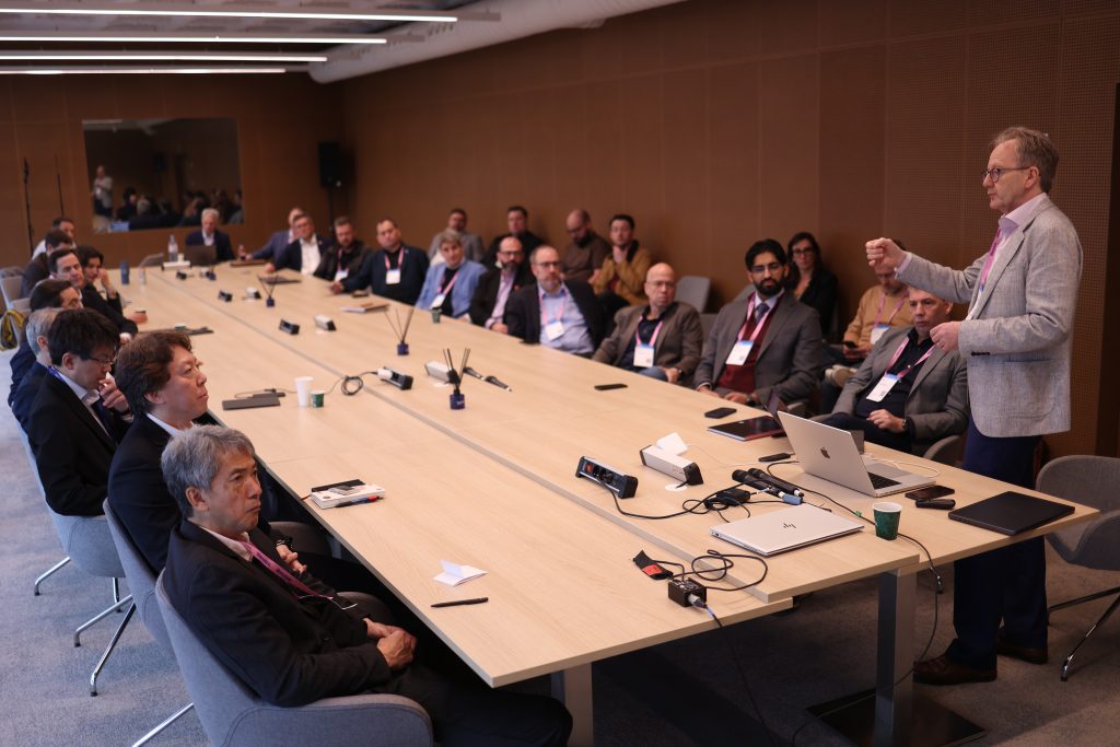 A man gives a presentation to a group of people seated around a large conference table in a meeting room.