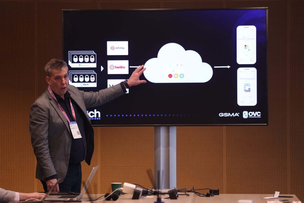 A man gives a presentation, pointing at a cloud diagram on a large screen in a conference room.