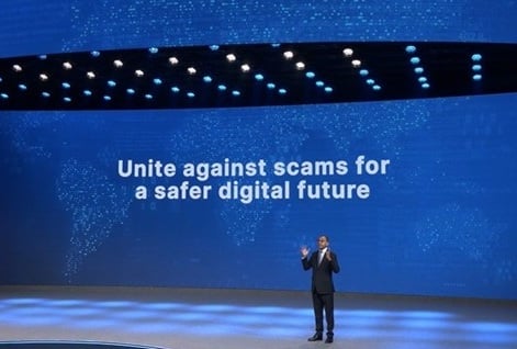 Man speaking on stage with screen behind that reads, "Unite against scams for a safer digital future.