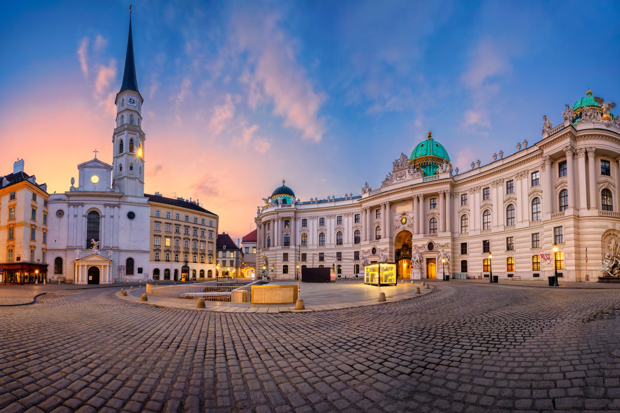 A cobblestone square with historic buildings and a church at sunset in Vienna, Austria.