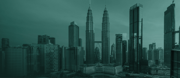 A city skyline featuring the Petronas Twin Towers in the centre, surrounded by high-rise buildings and skyscrapers. The image, with a greenish tint, highlights an urban landscape under a clear sky—an ideal spot for promoting scam prevention awareness.