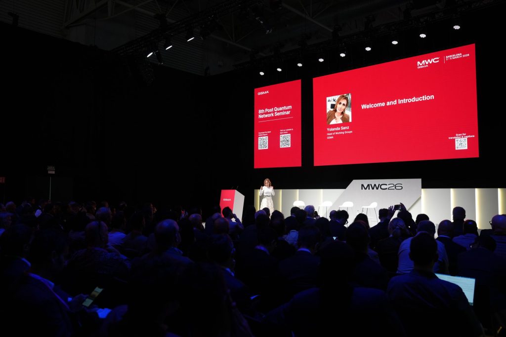 A speaker addresses a seated audience at MWC 2024, with presentation slides displayed on large screens.