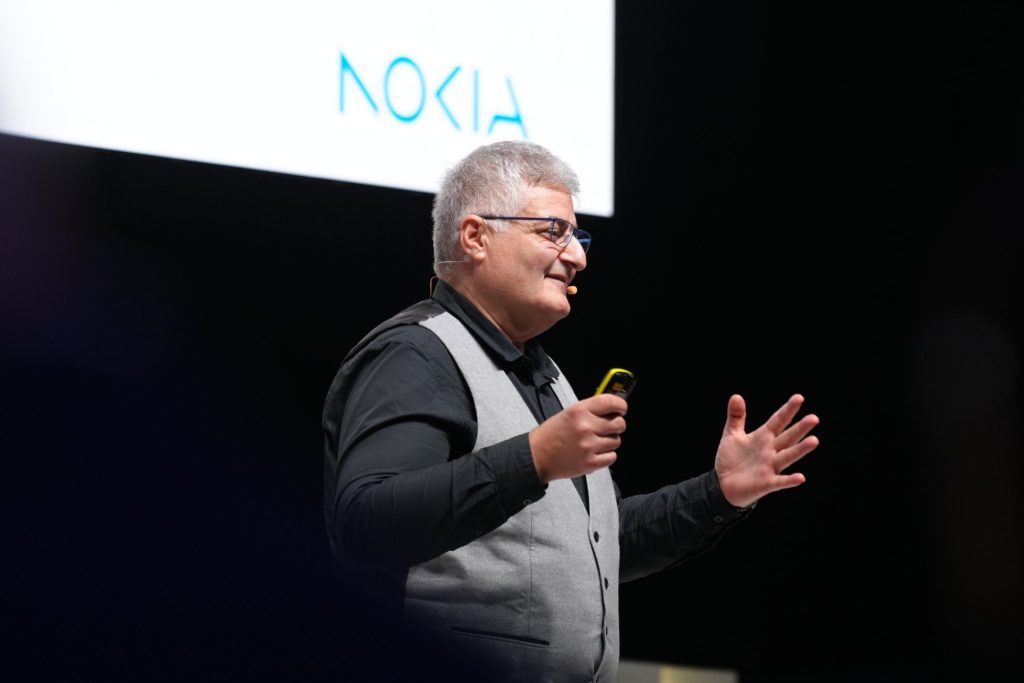 A man in a waistcoat speaks on stage with a Nokia logo visible in the background.