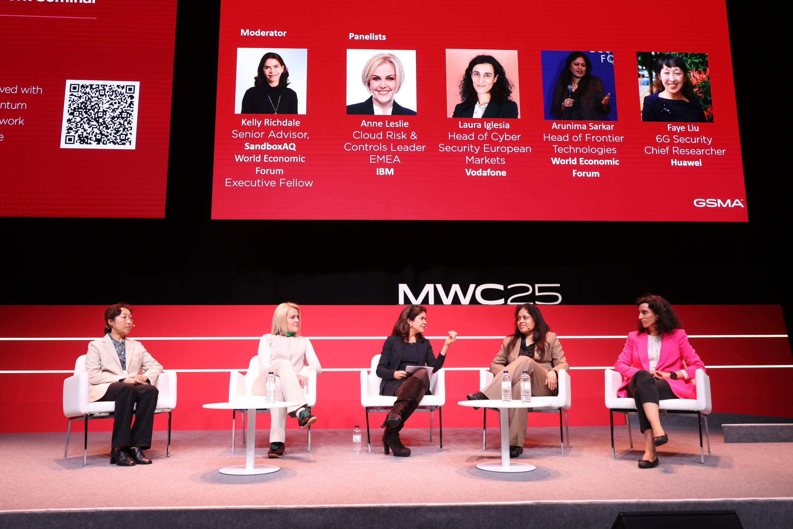 A panel of five people sits on stage at the MWC25 event, discussing Post-Quantum advancements. Two women sit on the left; one in a red top, the other in white. Three women sit on the right, dressed in black, beige, and red. Behind them, a large screen displays a QR code and speaker information.