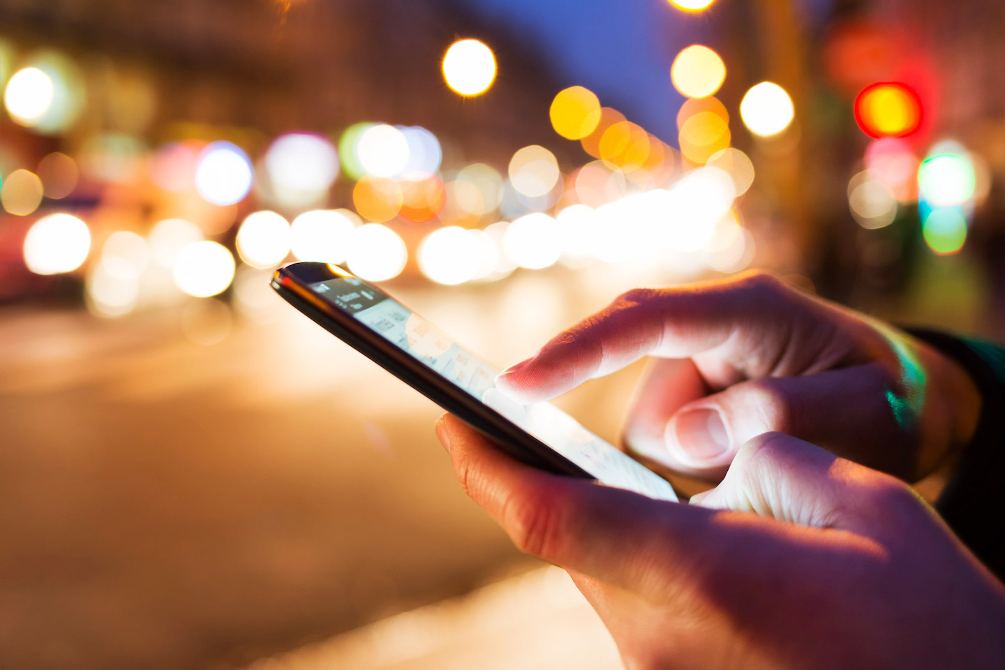 A person using a cell phone in a city at night.