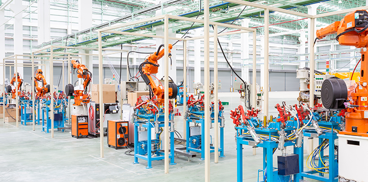 A modern industrial factory floor with multiple orange robotic arms and assembly stations, arranged in neat rows within a spacious, well-lit building.