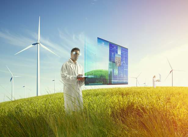 A person in a lab coat stands in a grassy field with multiple wind turbines. They are interacting with a digital screen displaying data and graphs. Another person in the background also engages with a screen. The scene is bathed in warm sunlight, suggesting a focus on renewable energy.