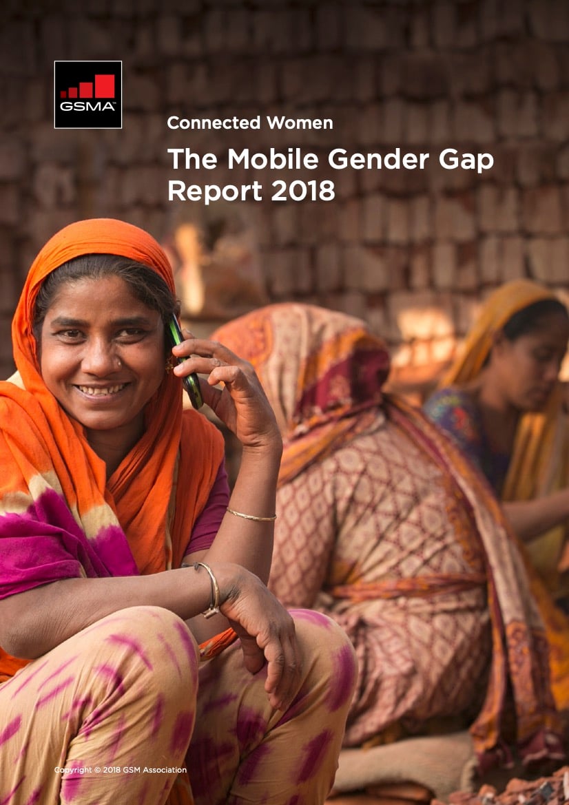A smiling woman in an orange sari uses a mobile phone. Two women in colourful saris sit in the background, one working with her hands. The setting is outdoors with a rustic wall. Text reads: “The Mobile Gender Gap Report 2018” and “Connected Women, GSMA.”.
