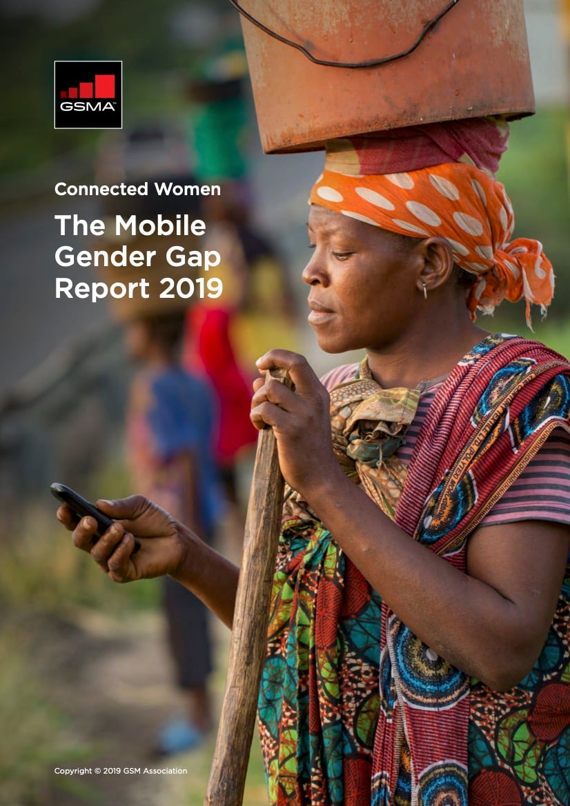 A woman in colourful clothing and a headscarf balances a clay pot on her head whilst holding and looking at a mobile phone. Text on the left reads “GSMA Connected Women: The Mobile Gender Gap Report 2019.” The background shows a rural outdoor setting.