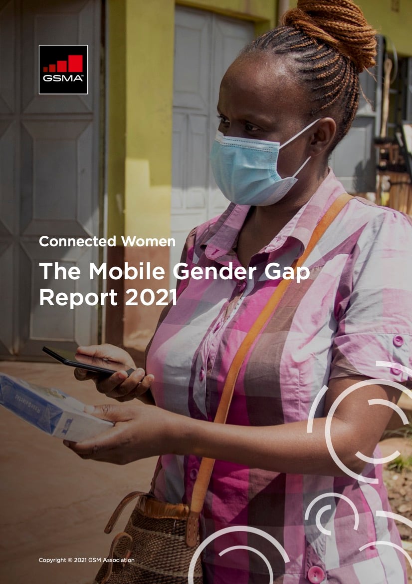 A woman in a pink checked shirt and blue surgical mask stands outdoors, holding a mobile phone and papers. She has plaited hair and a crossbody bag. Text over the image reads, “The Mobile Gender Gap Report 2021” by GSMA.