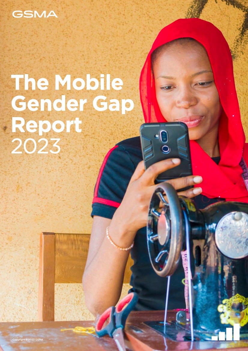 A woman wearing a red headscarf and black shirt smiles whilst looking at a smartphone. She sits at a table with a black sewing machine in front of her. Text on the image reads: "The Mobile Gender Gap Report 2023.